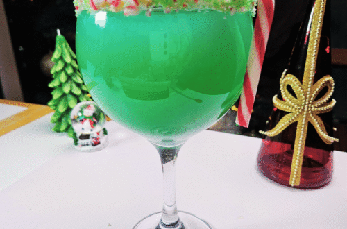 grinch mocktail with the rim of the glass garnished with green colored sugar and crushed candy cane