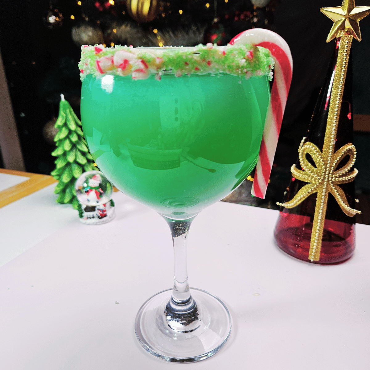 grinch mocktail with the rim of the glass garnished with green colored sugar and crushed candy cane